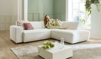 Frau sitzt beim telefonieren auf einem weißem Ecksofa mit Kissen